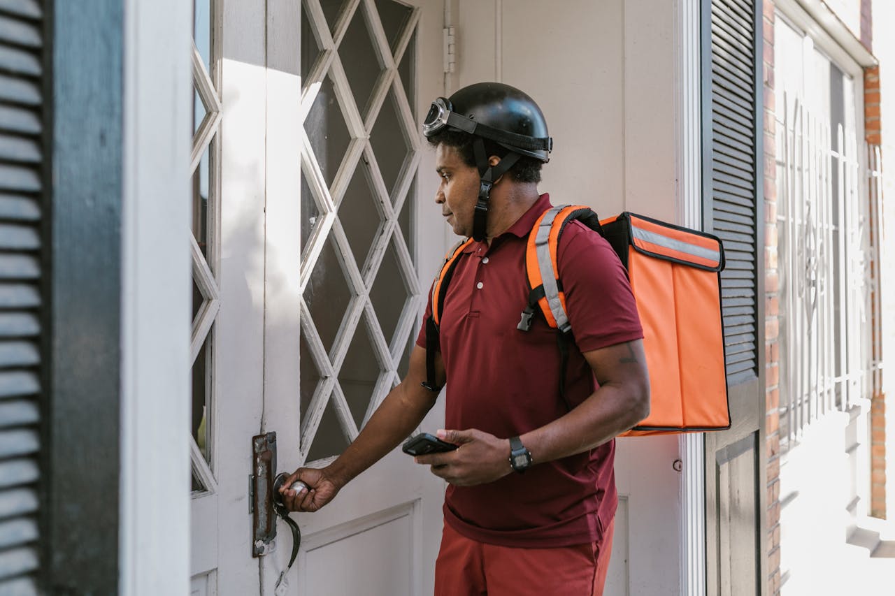 Delivery worker at a door during the day with an orange food backpack and helmet.
