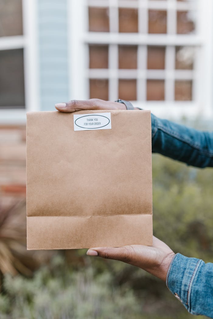 A person wearing a denim jacket holding a brown paper bag outside a windowed building